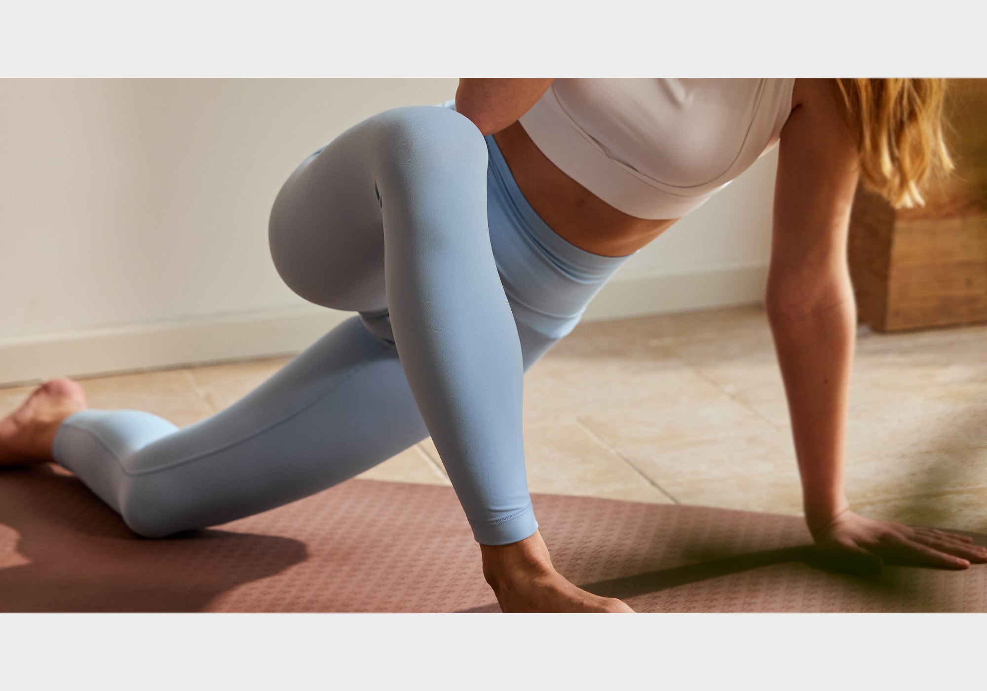 Person in light blue leggings and white top performing a yoga pose on a mat.