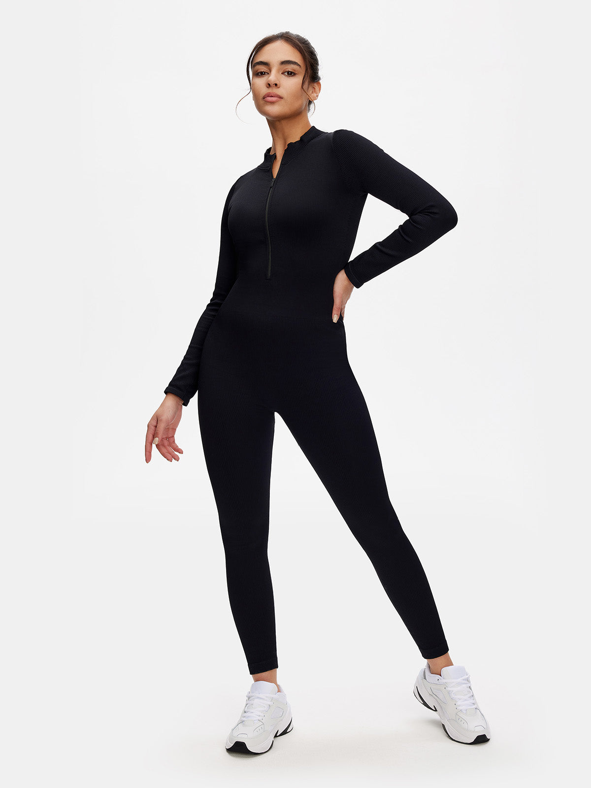 Woman wearing a black front zip-up long sleeve jumpsuit; ribbed bodycon fit with crew neck and sculpted silhouette.