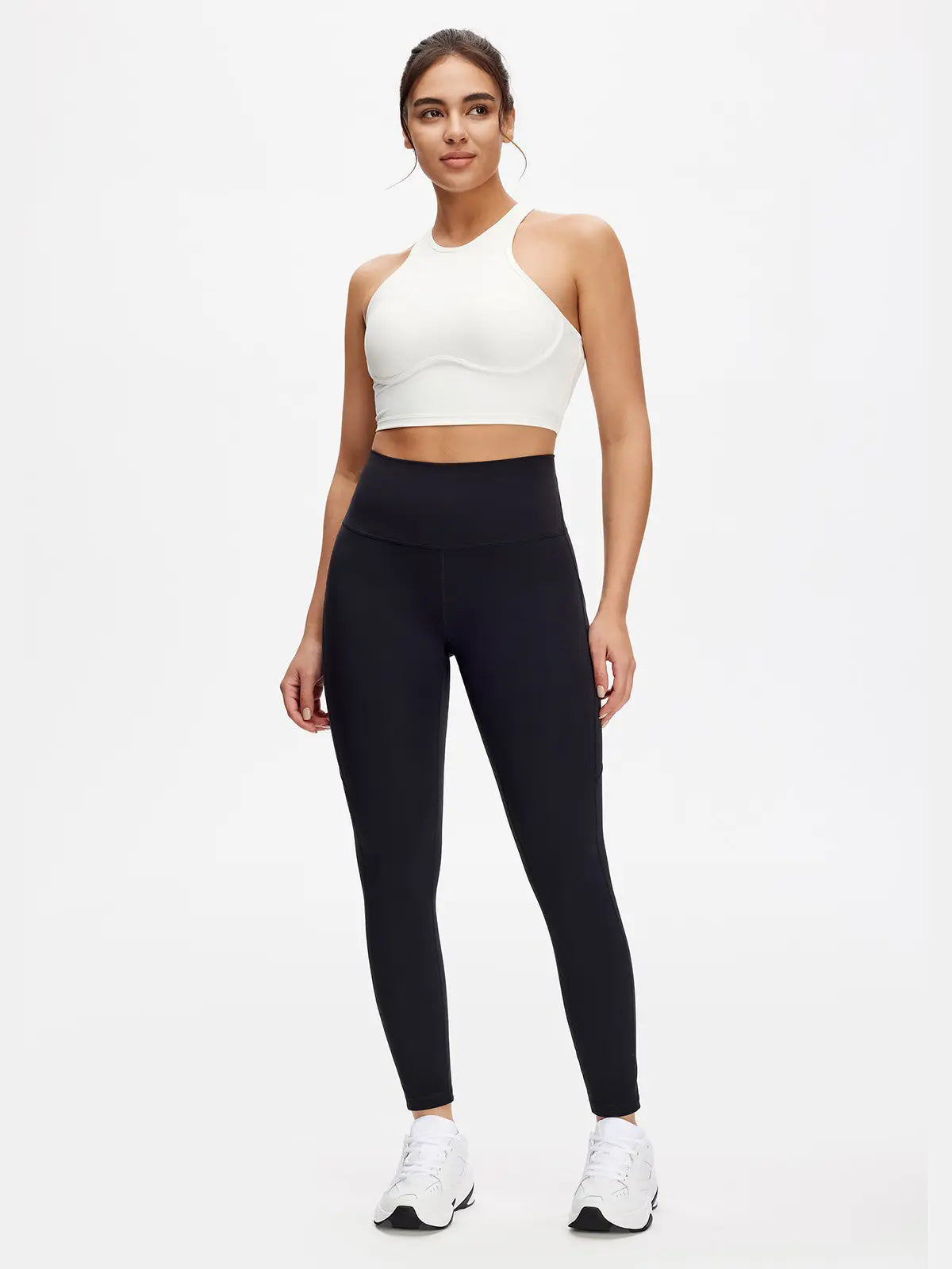 Woman wearing a white sports bra and black leggings on a white background