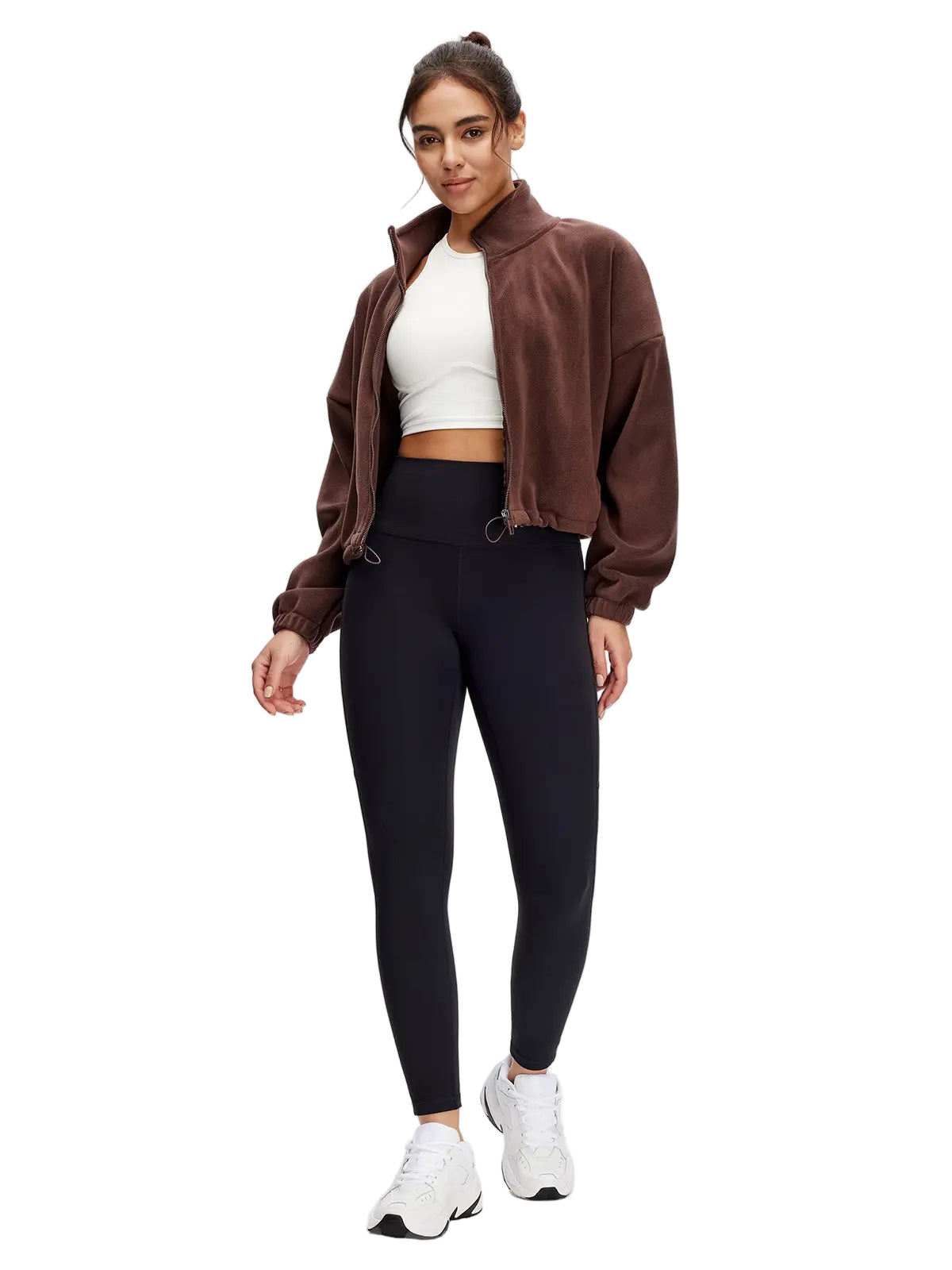 Woman wearing a brown jacket, white top, black leggings, and white sneakers on a white background