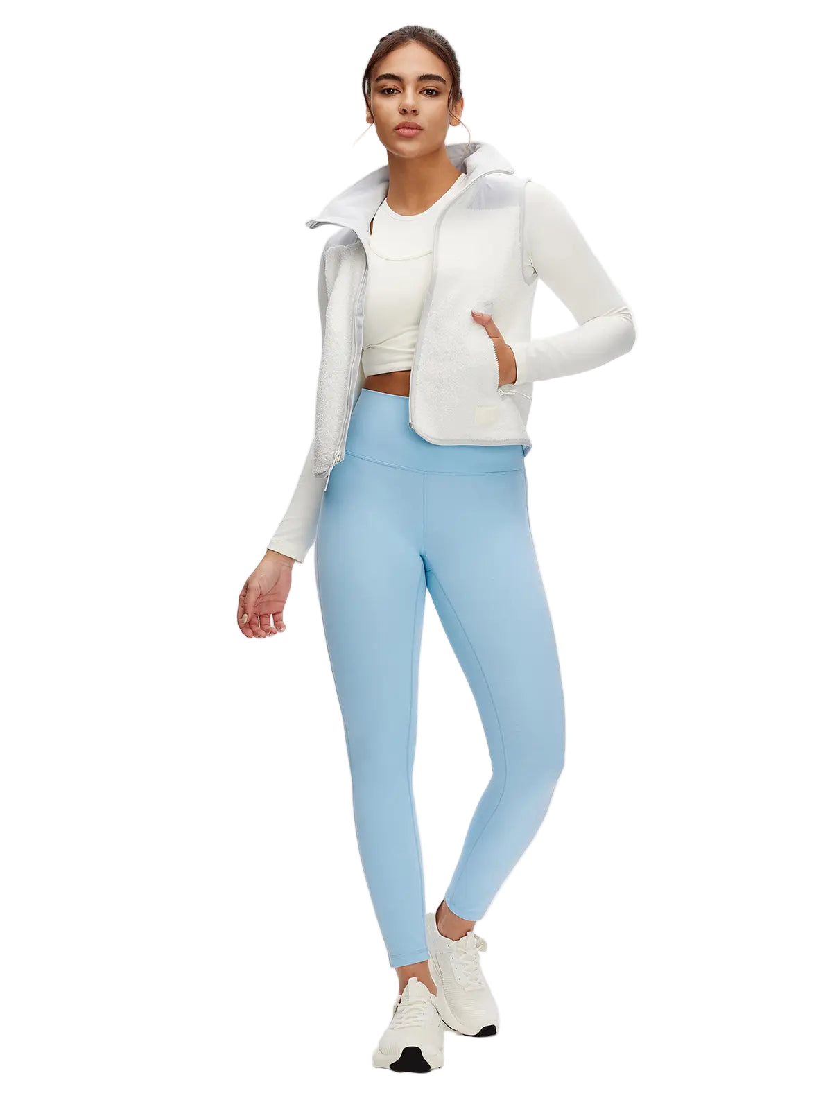 Woman wearing a white jacket, white crop top, and light blue leggings on a white background