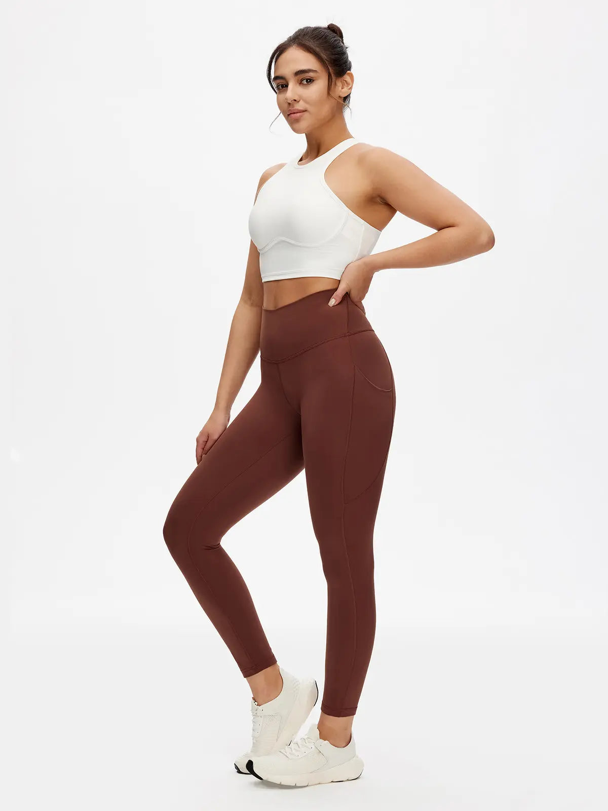 Woman wearing a white sports bra and brown leggings on a white background