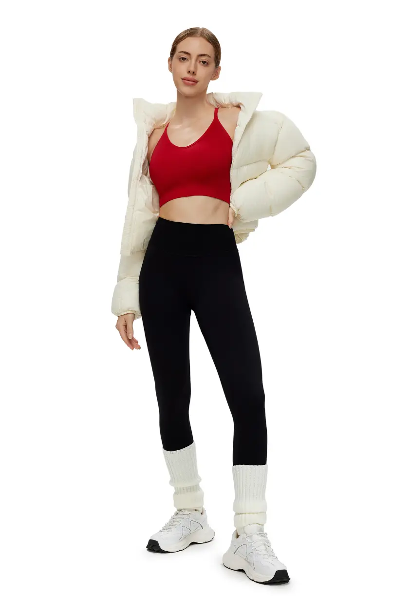 Person wearing a red sports bra, black leggings, white sneakers, and a cream puffer jacket on a white background